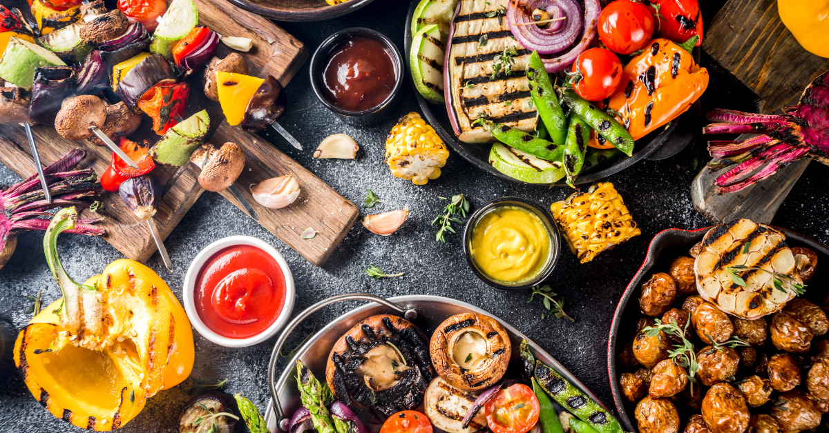 An aerial view of a black table with grilled meats, veggies, and assorted condiments on top