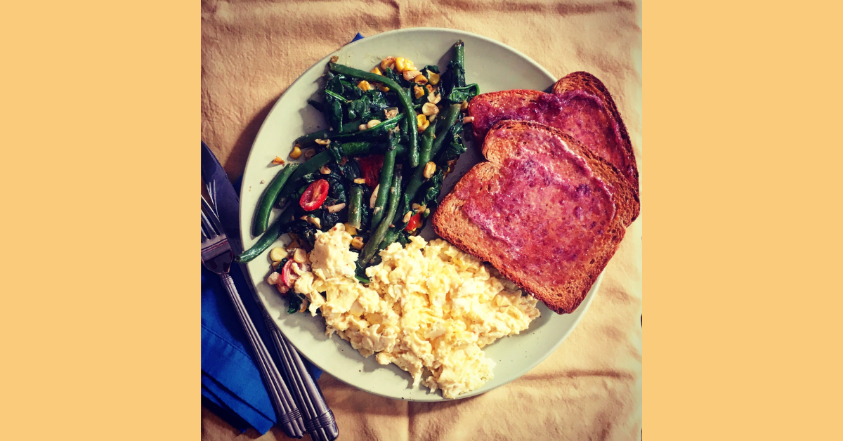 scrambled eggs, toast, and braised greens on top of a light green plate with a large yellow cloth napkin underneath