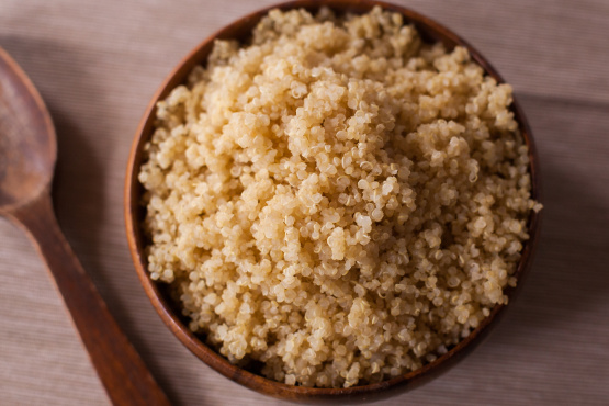 wooden bowl of cooked quinoa with wooden spoon on a table