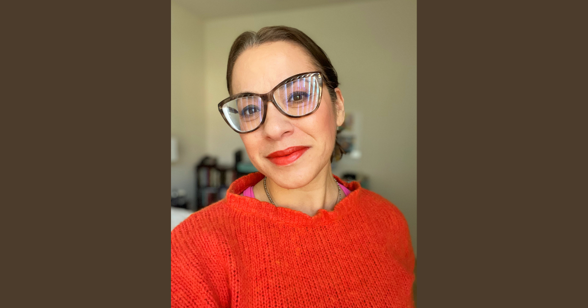Woman in glasses with orange sweater, bright red lipstick, soft smile
