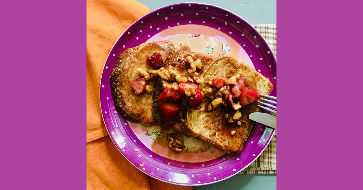 Three slices of French toast with berries and nuts atop a purple plate and orange napkin