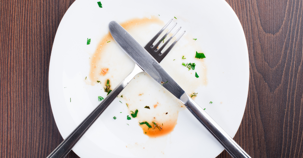 A white plate with some leftover sauce around the middle and criss-crossed fork & knife sitting atop