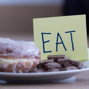 Plate of donuts and chocolate with a sticky note that reads "eat"
