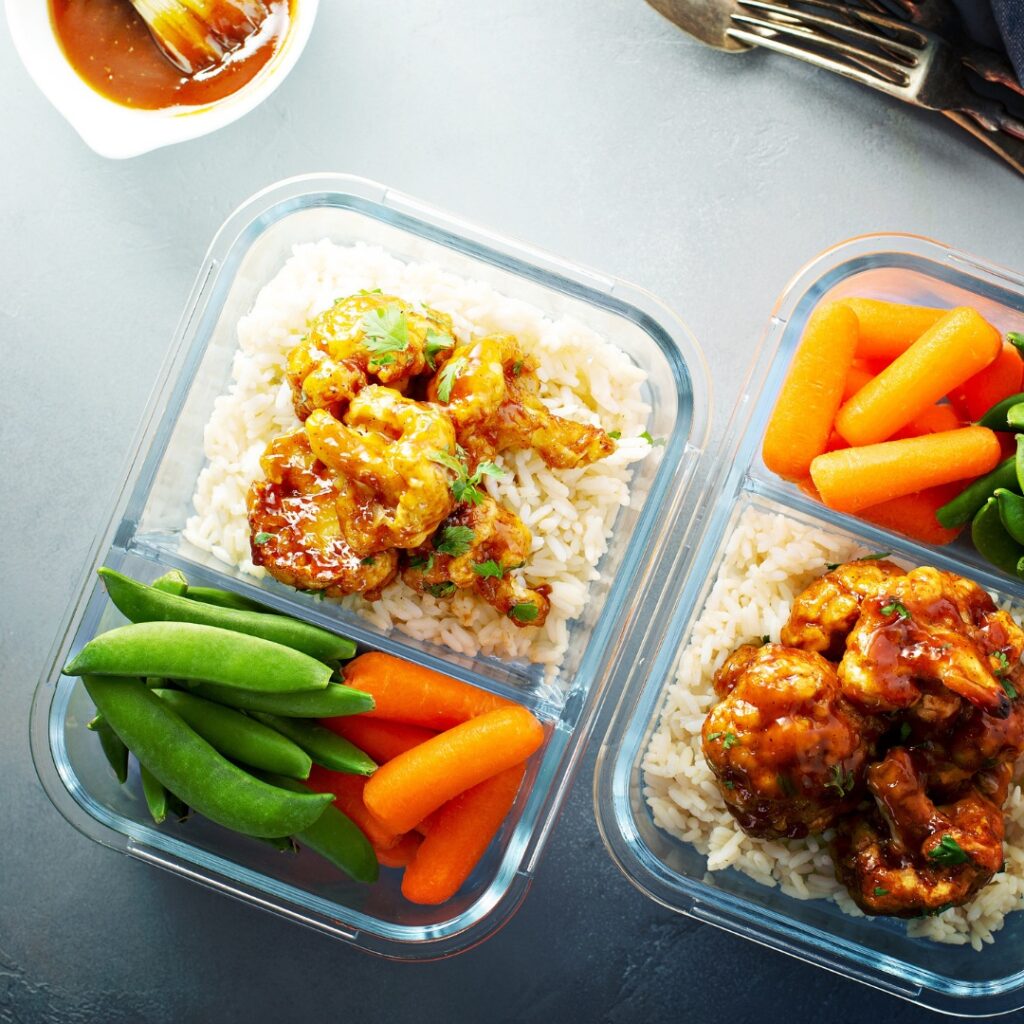 Table with glass containers of meal prepped food: shrimp over rice, vegetables