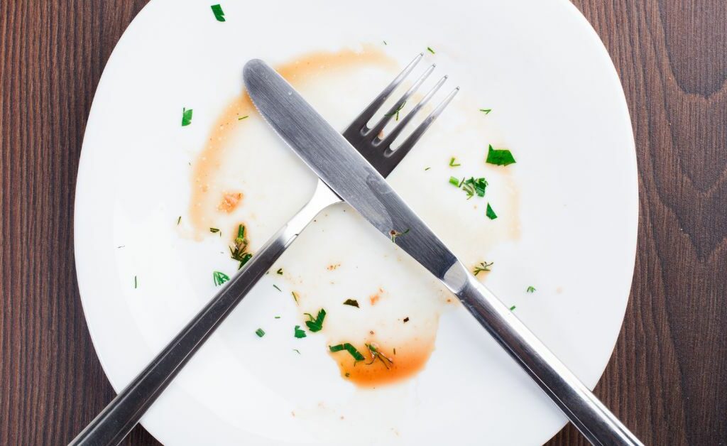 Picture of a dirty plate with a knife and fork placed on top in a criss-cross pattern.