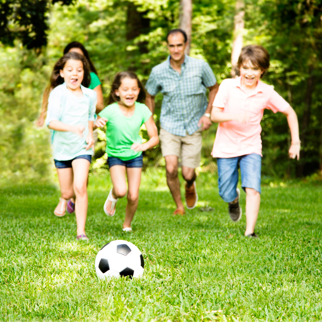Outdoor photo of grass with a group of people running after a soccer ball