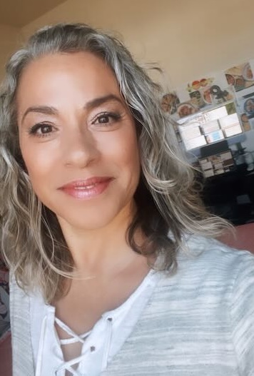 Dina in a green, white, and orange sweater, seated at desk, facing camera