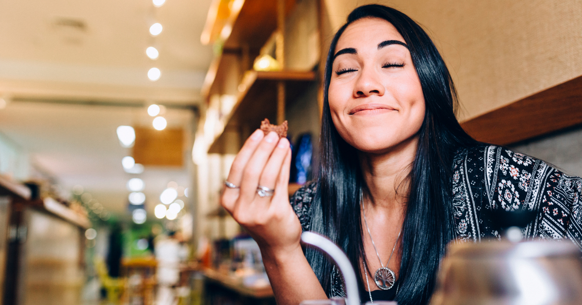 Woman with long dark hair, eyes closed and smiling, savoring a meal