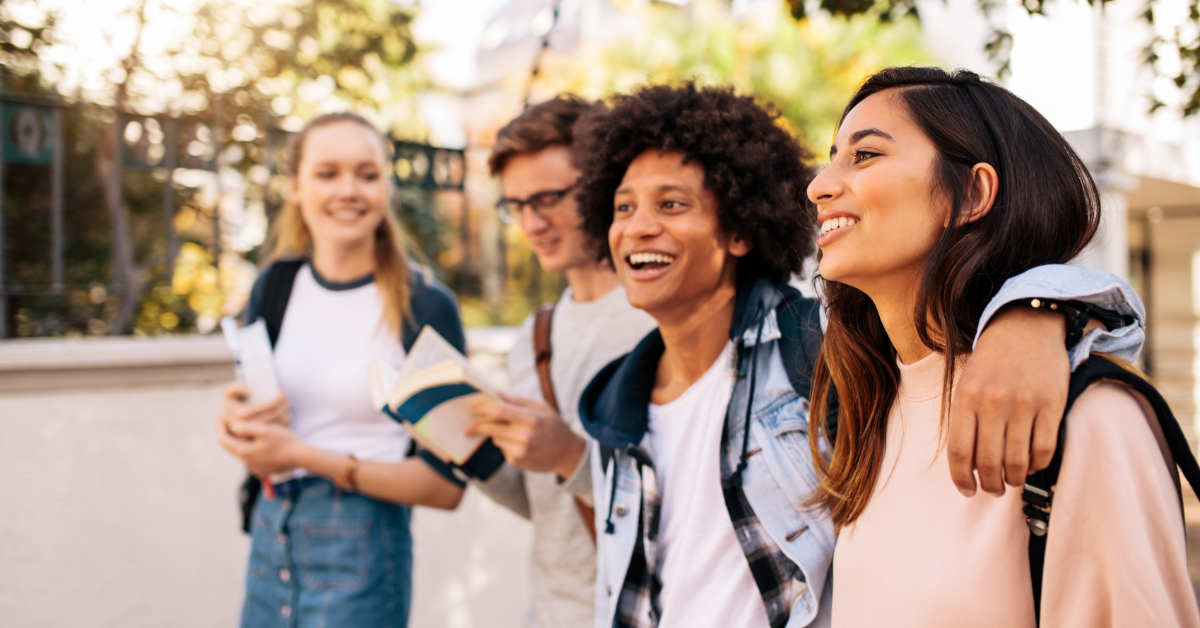 a diverse group of 4 college students are walking through campus smiling together